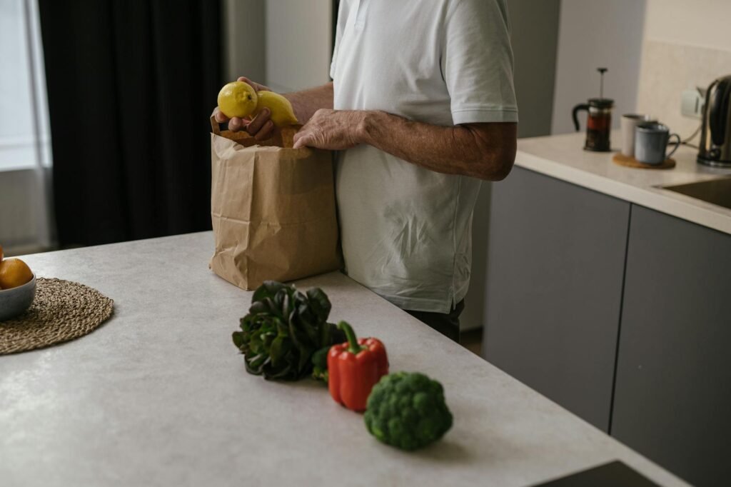 A grocery list, calculator, receipt, and vegetables arranged on a kitchen table